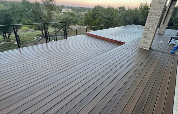 Installation of a Trex Toasted Sand composite deck with stainless steel cable railing, motorized deck cover, and integrated landscape lighting.