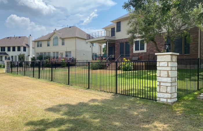 Completed ornamental iron fence framed by limestone block pillars.