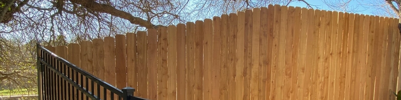 Finished vertical Western Red Cedar fence beside ornamental iron panels.