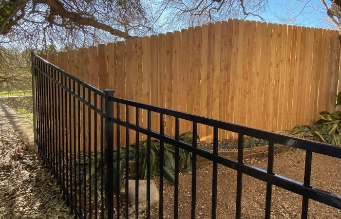 Finished vertical Western Red Cedar fence beside ornamental iron panels.