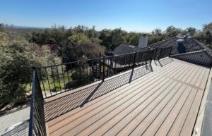 Installation of a rooftop deck using Trex Enhance Naturals deck boards in Toasted Sand, featuring a custom Trex bar, ornamental iron railing with flat top and bottom, and a spiral staircase built according to engineered plans.