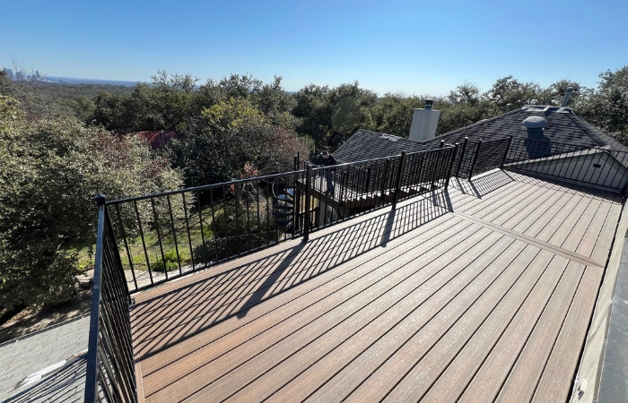 Installation of a rooftop deck using Trex Enhance Naturals deck boards in Toasted Sand, featuring a custom Trex bar, ornamental iron railing with flat top and bottom, and a spiral staircase built according to engineered plans.